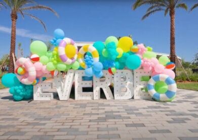 The Splashing Into Summer at EverBe in Orlando featured this sunny scene with a bright blue sky and palm trees in the background and giant white letters spelling EverBe crowned by a colorful balloon arch